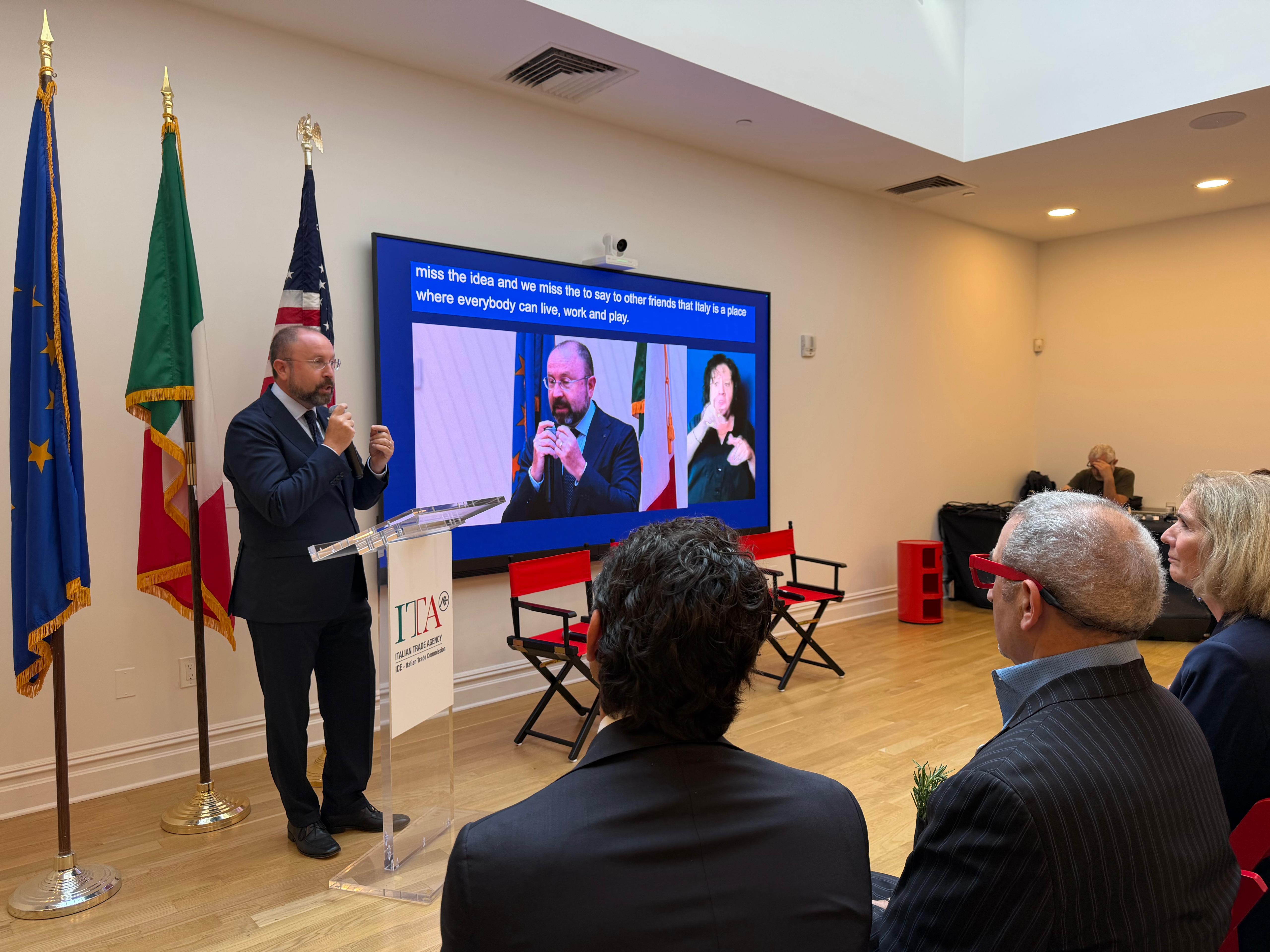 Relatore al podio durante il seminario internazionale sull’autismo del 10 settembre 2026 presso l’Italian Trade Agency di Manhattan, con pubblico in sala e contributo video proiettato sullo schermo.