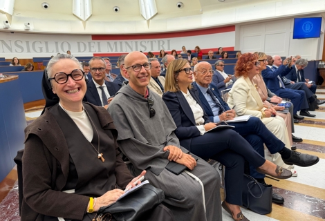 Partecipanti seduti nelle prime file della sala della PCM durante l’evento dedicato al secondo anniversario della Carta di Solfagnano. In primo piano, sulla sinistra, suor Veronica Donatello è seduta accanto ad altri ospiti e relatori. Sullo sfondo sono visibili il pubblico disposto nelle gradinate della sala e la grande scritta “Consiglio dei Ministri” che corre lungo la parete. L’ambiente è illuminato dalla caratteristica cupola con lucernari posta sopra l’aula.